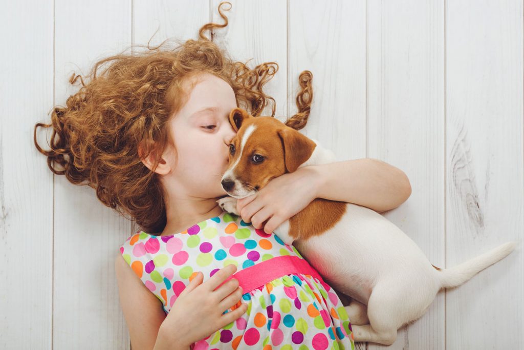 A little girl laying down with her puppy | Motif