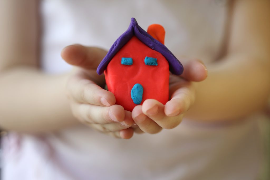 Take a closeup of your child holding house-shaped clay art for their art photo book.