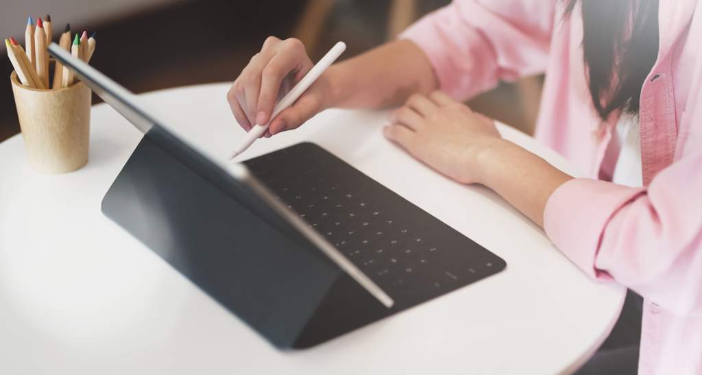 Woman in pink shirt uses Apple Pencil and Magic Keyboard to edit photos taken with iPad camera.