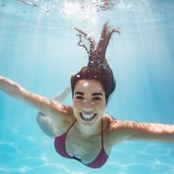 Young woman in red bikini smiles at camera during an underwater photography shoot.