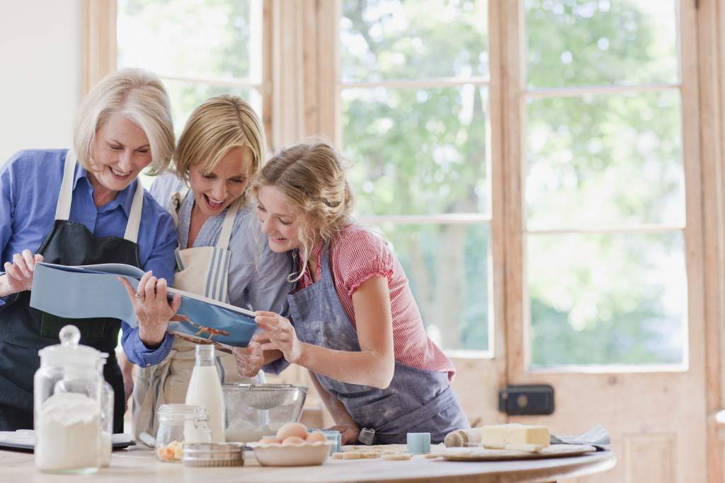 3 generations of women in the kitchen baking and looking at an Apple photo book with recipes.