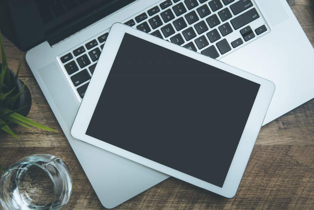 A Macbook and iPad on a wood desk are both devices you can use to create Apple photo book projects.